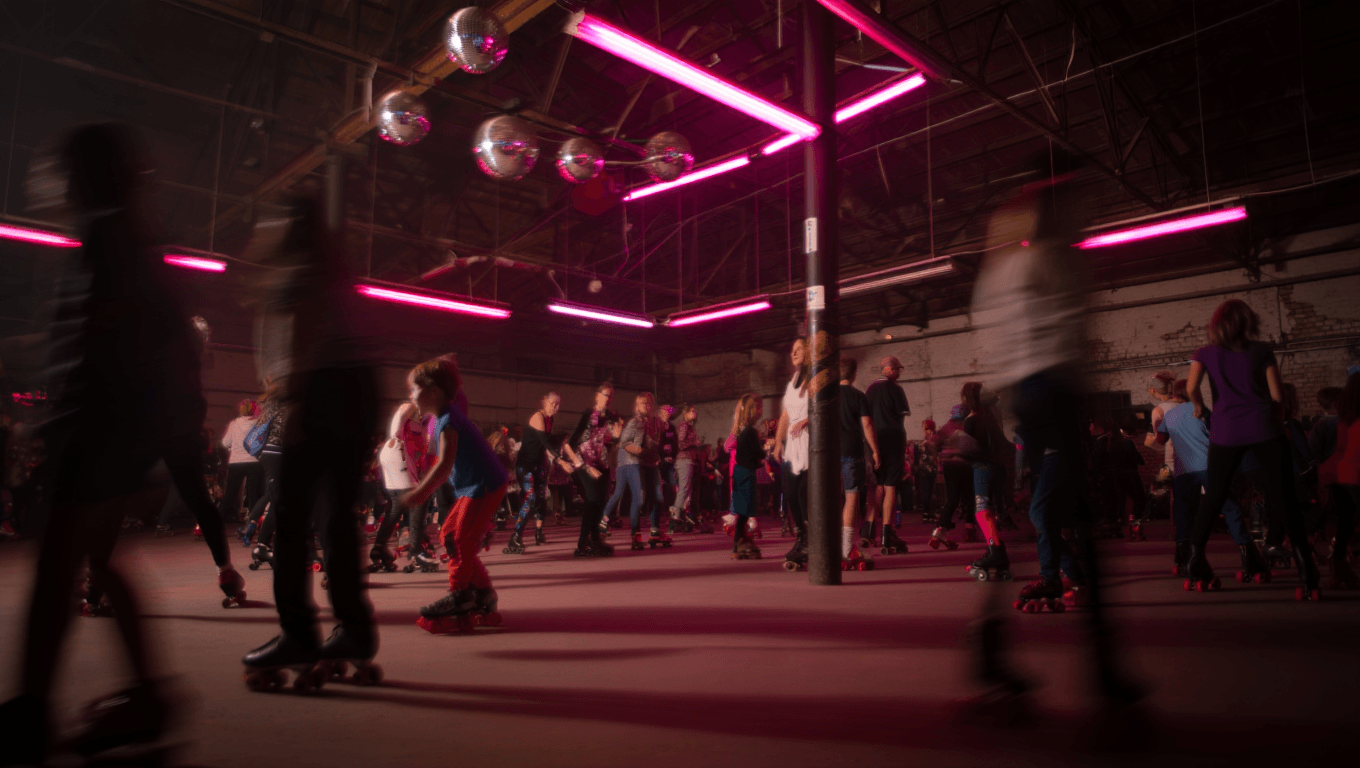 Roller skating rink with people of all ages roller skating around under neon lights